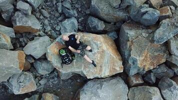 Bald Man lays on a large stone. Tourist with a backpack in shorts and t-shirt is resting. Aerial view video