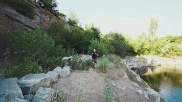 traveler is holding hands for the harnesses of a backpack and walking along the bank on the background of stones and rock. The tourist is looking at the wonderful landscape around him video