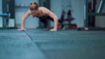 A strong woman with a ponytail push up from the floor in the gym. Blurred background. Camera motion forward video