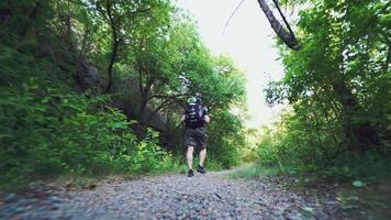 traveler in sportswear with backpack is walking along a path in the wood on the background of trees and rocks video