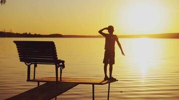 A little kid is standing on the masonry near the bench. The guy is looking around the area at sunset near the lake in the summer. video