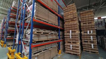 High metal shelves of blue color are filled with wooden boards in the building of a warehouse of a woodworking factory. View of the large storage of parquet from inside video