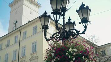 view of the decorative lantern which decorated with flowerpots with purple and white flowers on the background of the building in the city. Camera motion to side video