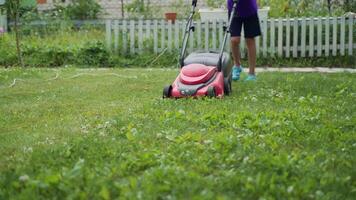 Boy running with a lawn mower in the garden. Mowing grass in the garden. Close-up video