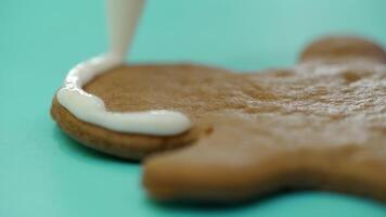 A confectioner is drawing a contour on ginger biscuits by white icing with using a confectionary nozzle for Christmas. Ginger man. Sweets. Close-up video