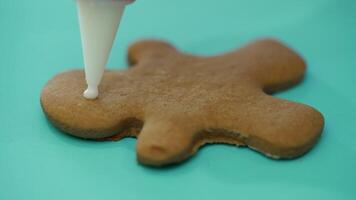 The confectionery nozzle is drawing the image of a person on the finished ginger biscuits with icing. Close-up. Christmas cookies video