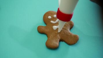 Hand of human is decorating by white glaze gingerbread biscuit with using brush bits on a turquoise background for Christmas. Close-up video