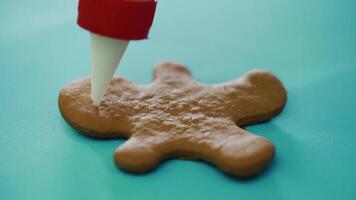 confectioner is painting cookies in the form of a ginger man on the New Year on the table in the kitchen. The process of decorating by glaze. Close-up video