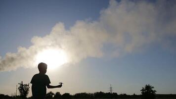 Child Playing With Airplane. Small boy playing with paper airplane at sunset near smoky pipes video