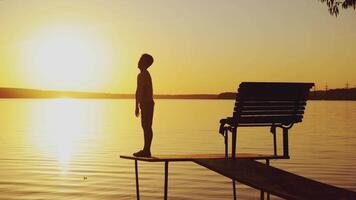 boy are doing physical activities on the bridge near the bench on the background of sunset by the river video