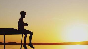 child is sitting on the end of the masonry and throwing pebbles into the water at sunset video