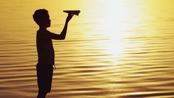 little boy holds a paper airplane in his hand at sunset. A child raised his hand up to sky and plays with origami in the evening in the street video
