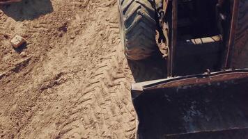 bulldozer with huge wheels and a bucket is moving around the territory of a sandy quarry. Close-up video
