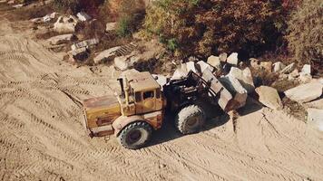 specially equipped machine with a bucket id working near a quarry with stones on the background of sand. video