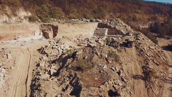 Arbeitskräfte mit Fachmann Ausrüstung sind Arbeiten im das sandig Steinbruch auf das Hintergrund von enorm Steine und ein Hügel mit Bäume. Kamera Bewegung oben video