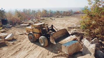 professional yellow bulldozer with a bucket is working in the quarry with stones on the background of sand. Close-up video