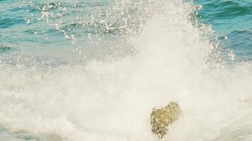 high sea waves of turquoise color are crashing on the rocks and turning into foam. Slow motion video