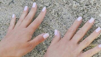 hands of the woman are leaving traces of palms on sand on the shore of sea in the summer. Close-up video