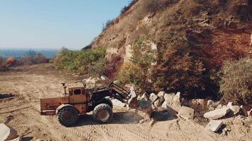 specially machinery with a bucket for picking stones is working in a quarry near the hill with forest. Close-up video