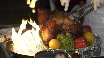 chef is cutting the baked chicken with a knife and putting the slices on the plates near the fire in the street on the summer terrace of the cafe video