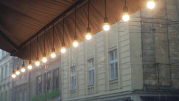 view on a row of burning light bulbs from the roof of a restaurant on the background of raindrops from the street. It's raining video