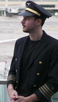 A pilot in uniform stands confidently at the bustling airport terminal ready for duties video