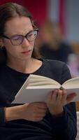 un joven mujer profundamente comprometido en el alegría de leyendo un libro en un moderno biblioteca ambiente video