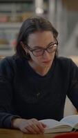 A focused woman deeply engaged in reading a book in the calming and quiet setting of a library video