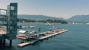 Vancouver Canada 20.09.2024 Harbour Flight Centre. Seaplanes docked at harbor with mountainous backdrop. A view of seaplanes docked at a harbor with a backdrop of mountains and a bustling waterfront. video