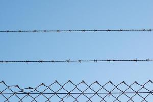 view of a wire fence with barbed wire on top of it on a blue sky day photo