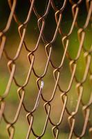 Close up of chain link fence with blurred landscape and setting sun in the background, selective focus photo