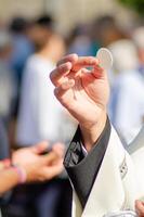hand of a catholic priest elevating the host in the sacrament of communion at an outdoor service photo