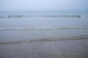 View of the shore of a beach with smooth waves on a cloudy day. photo