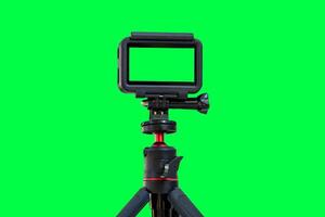 Action camera with empty screen on a mini tripod. Action cam installed on tripod with green screen background photo