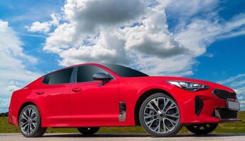 Red car on a blue sky background with white clouds. A stylish, modern, bright image of an avto mobile for design solutions. photo