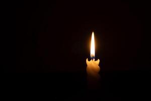 A single burning candle flame or light glowing on a spiral white candle on black or dark background on table in church for Christmas, funeral or memorial service with copy space photo