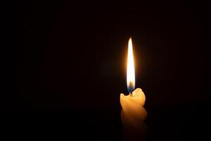 A single burning candle flame or light glowing on a spiral white candle on black or dark background on table in church for Christmas, funeral or memorial service with copy space photo