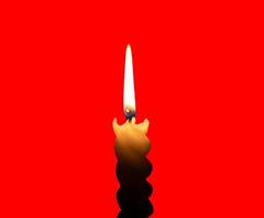 A single burning candle flame or light glowing on a small spiral white candle isolated on red background with clipping path photo