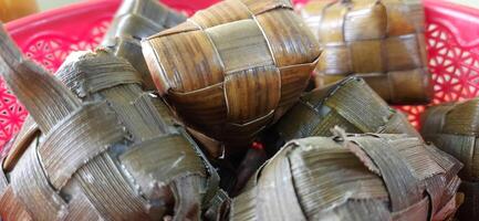 Ketupat or rice dumpling packed inside a diamond-shaped container of woven palm leaf pouch. Special dish served at Eid Mubarak Ied Fitr celebration in Indonesia photo
