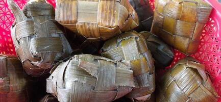 Ketupat or rice dumpling packed inside a diamond-shaped container of woven palm leaf pouch. Special dish served at Eid Mubarak Ied Fitr celebration in Indonesia photo