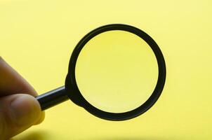 Hand holding magnifying with yellow background and with customizable space for text or ideas photo
