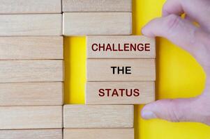 Hand pulling out wooden blocks with Challenge the Status text on yellow background. photo