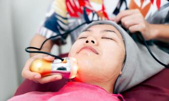 A woman is getting a facial treatment with a device that is emitting a light photo