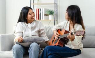 Two women are sitting on a couch, one of them playing a guitar photo