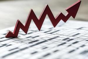 A striking red downward arrow pierces through a printed financial chart, symbolizing a sudden drop in market trends. The chart lies on a wooden table, emphasizing the severity of the decline. photo