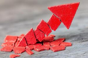 A bright red downward arrow crashes through fragmented pieces on a wooden surface, signifying a sharp decline or setback. The dynamic impact emphasizes failure and disruption in growth. photo