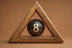 A solitary black snooker ball with the number eight is placed inside a triangular wooden rack, set against a smooth, neutral backdrop, creating a minimalist aesthetic. photo