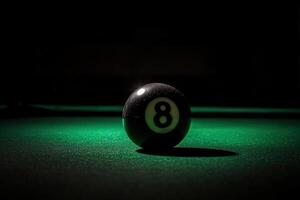 A single black snooker ball lies perilously on the edge of a green felt surface, illuminated by soft lighting that highlights its glossy finish and the surrounding shadows. photo