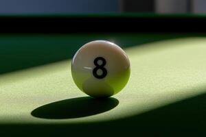 A single snooker ball, numbered eight, sits precariously on the edge of a green felt table. Soft sunlight casts a gentle shadow, highlighting its glossy surface and creating a serene atmosphere. photo