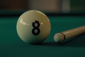 A solitary snooker ball, numbered eight, is positioned next to a sleek cue stick on a vibrant green felt table, emphasizing the focus of the game and its quiet anticipation. photo